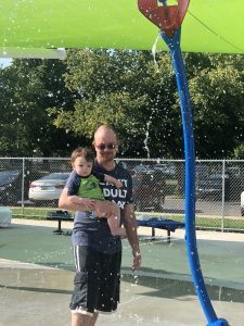 Matt holding Shiloh under a flower sprinkler