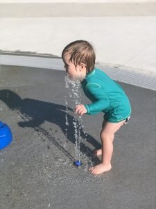 Asher bending over sprinkler washing his throat and chin