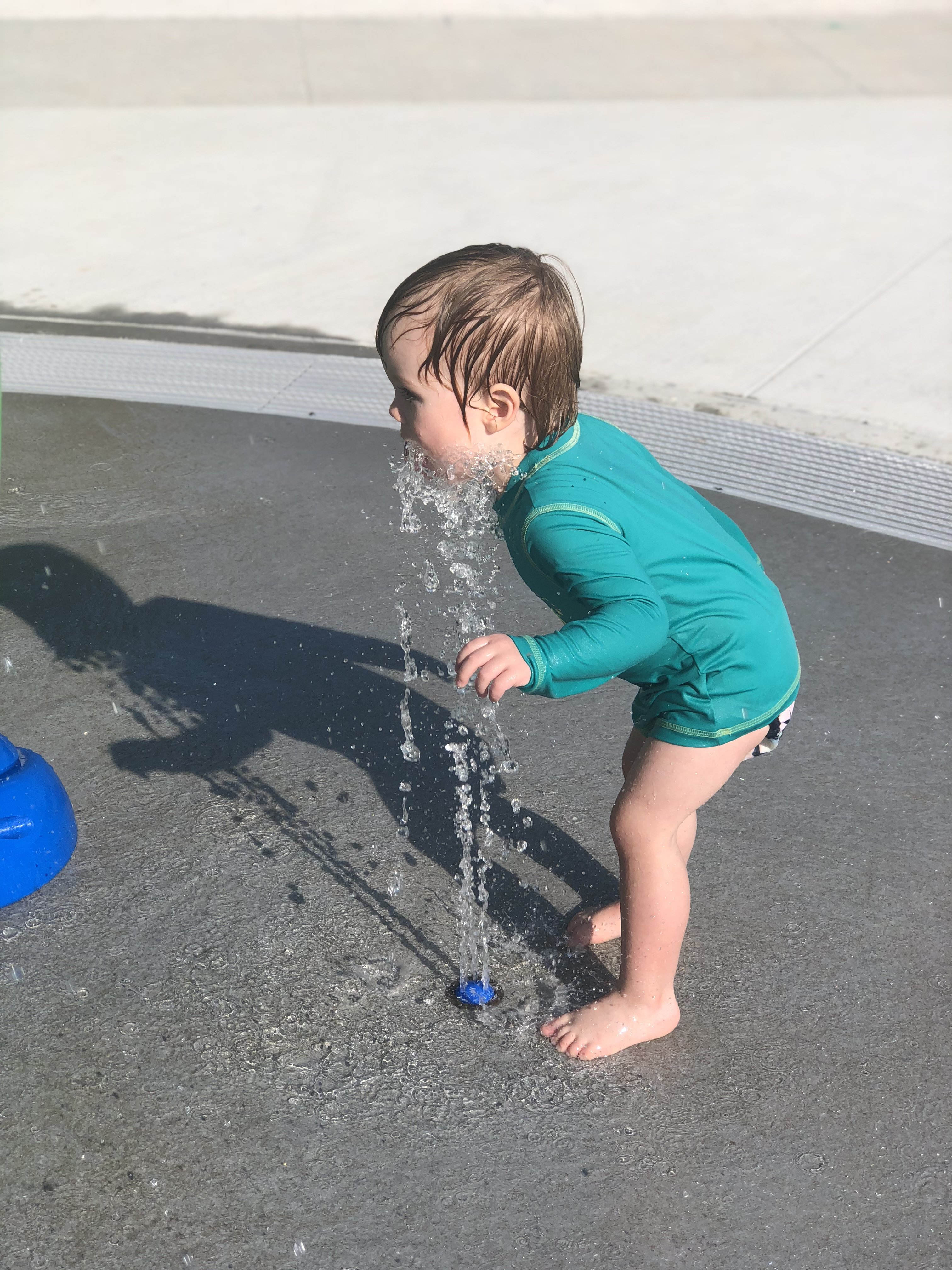 Asher bending over sprinkler washing his throat and chin